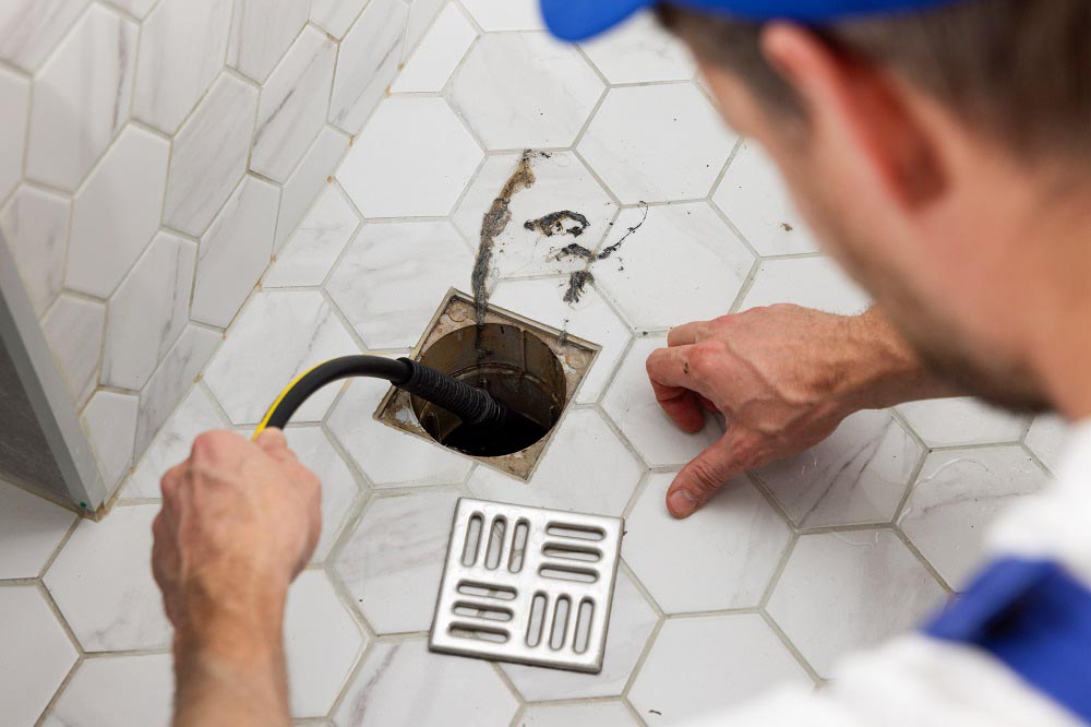 plumber unclogging blocked shower drain with hydro-jetting